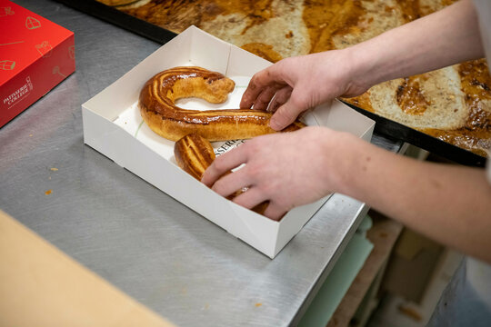 A person's hands arranging a large twisted pastry inside a white box on a kitchen counter.