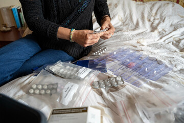 Person organizes assorted medications on a bed, sorting pills into a weekly pill organizer.