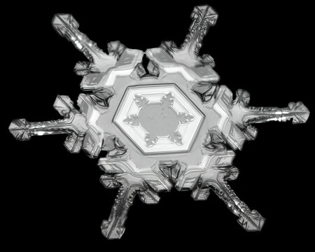 Close-up of a single snowflake displaying intricate patterns and symmetrical branches on a dark background.