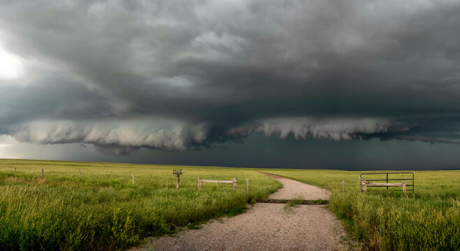 Ominous shelf cloud looms over a serene rural landscape with a gravel path leading towards the impending storm.