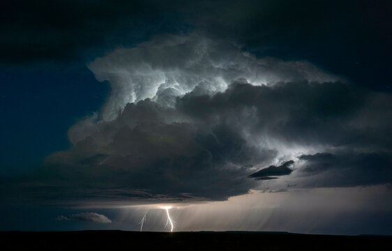 Lightning strikes illuminate a towering cumulonimbus cloud against the night sky.