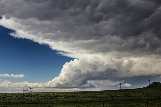 Dark storm clouds gather above a wind farm on a vast open plain, heralding an approaching storm.