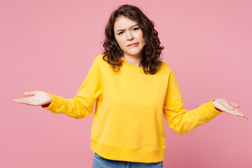 Young sad woman she wears yellow sweatshirt casual clothes spread hands shrugging shoulders looking...