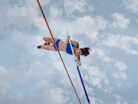 Female athlete vaulting over a high bar against a cloudy sky background.