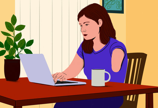 A woman with a limb difference seated at a desk focused on typing on her laptop with a coffee mug and indoor plant beside her.