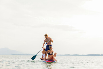 Three friends enjoy paddleboarding on a serene lake, with mountains faintly visible in the background under a soft sky.