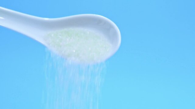 Slow motion video of sugar crystals falling out of ceramic spoon