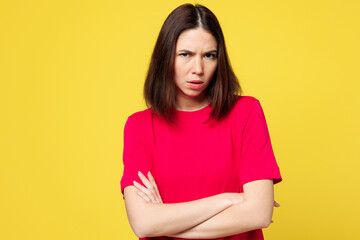 Obraz premium Young sad frowning mad woman she wearing pink t-shirt casual clothes look camera hold hands crossed folded looking camera isolated on plain yellow orange background studio portrait. Lifestyle concept.