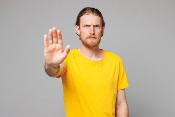 Young sad mad serious strict Caucasian man he wearing yellow t-shirt casual clothes showing stop gesture with palm looking camera isolated on plain grey background studio portrait. Lifestyle concept.