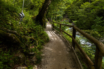 Fototapeta premium Vintgar Gorges Park a few km from Lake Bled, Slovenia. Wooden walkways accompany the path above the river rapids and waterfalls. River hits rocks and creates fog.Adventure family holidays. Freshness.