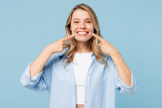 Young smiling satisfied happy woman she wearing white top shirt casual clothes point index fingers on opened mouth teeth isolated on plain pastel light blue cyan background studio. Lifestyle concept.
