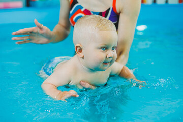 Little boy in the pool. A baby learns to swim with a coach in the pool. Swimming courses for small children. Swimming pool for children