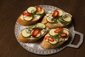 Сheese and cucumber baguette canapes on a metal board