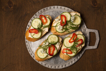 Сheese and cucumber baguette canapes on a metal board, top view