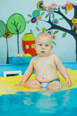 A baby learns to swim with a coach in the pool. Swimming courses for small children. Baby boy swims in the pool.