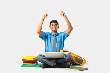 Asian Indian schoolboy with books and laptop, pointing at blank space, promoting education