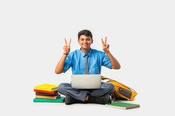 Asian Indian schoolboy with books and laptop, pointing at blank space, promoting education