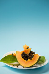 Ripe juicy papaya in a white plate on a blue background, copy space