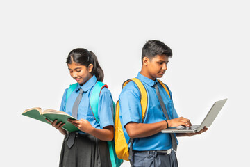 Asian Indian schoolboy and schoolgirl in uniforms, presenting blank space with books and backpacks