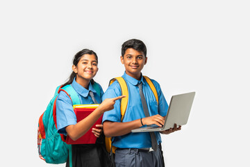 Asian Indian schoolboy and schoolgirl in uniforms, presenting blank space with books and backpacks