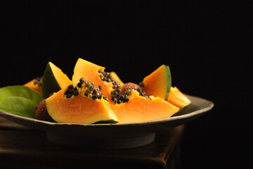 Sliced ​​ripe papaya with lychee in a handmade ceramic bowl on a black background