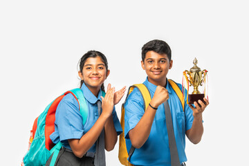 Indian asian schoolboy and schoolgirl in uniforms, holding trophy, celebrating achievement