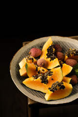 Sliced ​​ripe papaya with lychee in a handmade bowl on a black