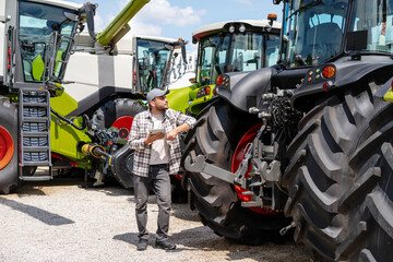 Farm machinery dealer. A man with a digital tablet stands at an agricultural equipment dealer and...