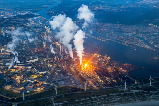 Aerial image of steel plant, factory, refinery with massive flame from chimney. Generating, producing steel and metal from coal and iron ore in IJmuiden Netherlands during evening alongside North Sea 