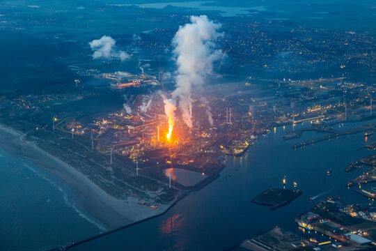 Aerial image of steel plant, factory, refinery with massive flame from chimney. Generating, producing steel and metal from coal and iron ore in IJmuiden Netherlands during evening alongside North Sea 