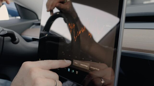 A close-up view of a man's hand interacting with an electric car's touchscreen. He is checking the battery range and statistics, focusing on energy efficiency and vehicle performance.
