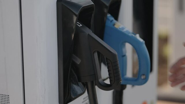 Close-up view of an electric vehicle charging station, featuring black and blue charging connectors. Emphasizes modern electric transportation infrastructure.