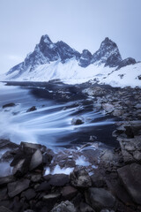 Vertical shot Eystrahorn mountain in Iceland on a gloomy dark evening during winter, waves on the black beach, volcanic landscape