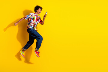 Fototapeta premium Full body portrait of nice young man jump run smart phone wear shirt isolated on vivid yellow color background