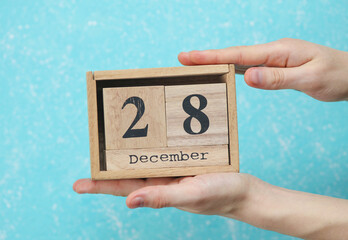 woman's hand holds wooden block calendar with the date December 28 on blue concrete background