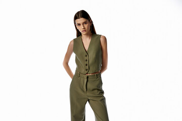 Fototapeta premium A beautiful woman with long dark hair poses in a stylish green jumpsuit against a gray backdrop, exuding elegance and sophistication.