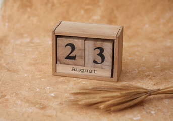 Wooden block calendar with the date August 23 and spikelets of wheat on a beige concrete background