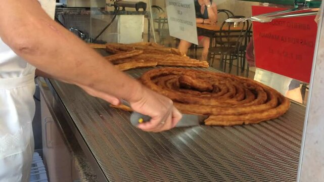 Unrecognizable man works in a traditional Spanish churreria cutting a "rosca" of fried dough into "porras".