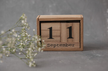 Wooden calendar with the date September 11 and gypsophila flowers on a gray concrete background