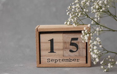 Wooden calendar with the date September 15 and gypsophila flowers on a gray concrete background