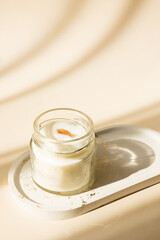 Handmade candle from paraffin and soy wax in glass with wooden wick isolated on pastel beige background. Flat lay, top view, copy space