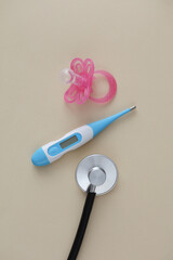 Stethoscope, electronic thermometer and pacifier for newborns on a beige background. Pediatric medicine