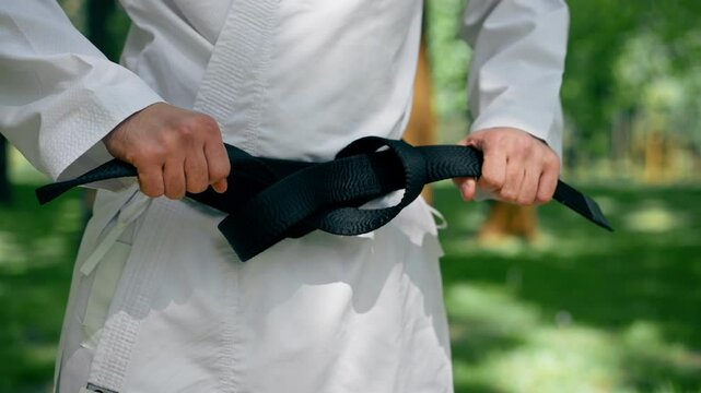 close up outdoors in the park in sunny weather a young karate guy tightens his belt using the karate technique martial arts black belt healthy lifestyle