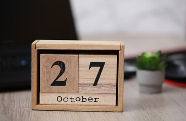 Wooden calendar with the date October 27 on desktop with laptop