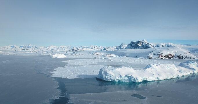 Amazing winter wild nature landscape in Antarctica. Snow covered icebergs and mountain range under blue sky. Frozen polar ocean surface background. Antarctic travel, exploration. Discover South Pole