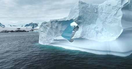 Antarctic landscape large iceberg with melted hole drifts polar ocean. Snow covered mountains in background. Winter nature environment. Ecology, melting ice, climate change and global warming concept © mozgova
