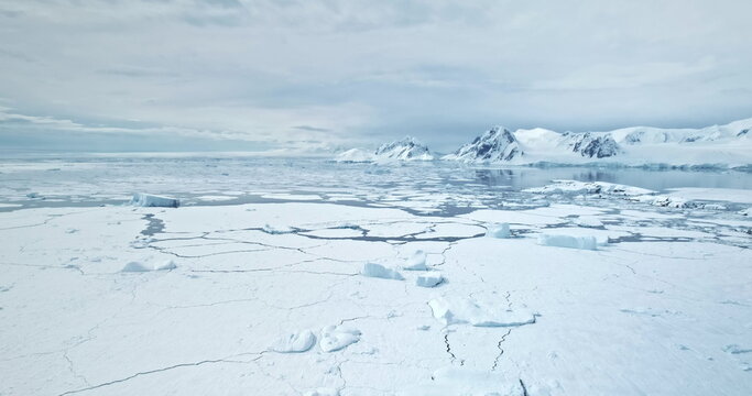 Rise up aerial panorama over winter polar landscape. Snow covered field, frozen ocean with icebergs and melting ice floes, mountain range in background. Discover beauty of Antarctica, travel, explore