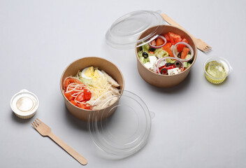 Greek and Caesar salad in disposable cardboard containers on a gray background