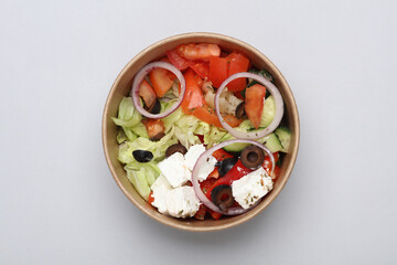 Greek salad in a disposable cardboard container on a gray background