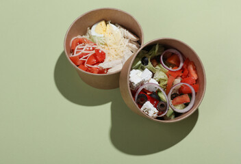 Greek and Caesar salad in disposable cardboard containers on a green background